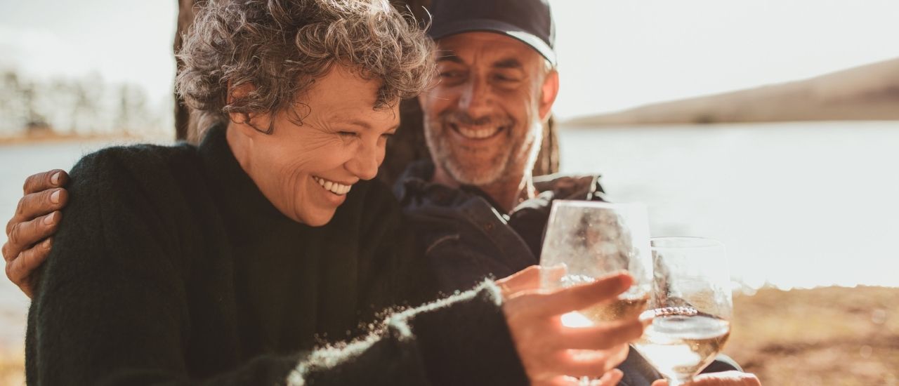 Couple with water glasses resting along riverbank